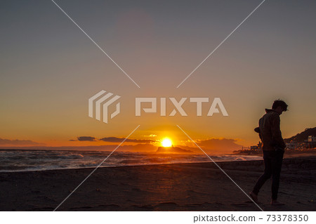 Man walking on the sandy beach at dusk Man walking on the sandy beach at dusk 73378350