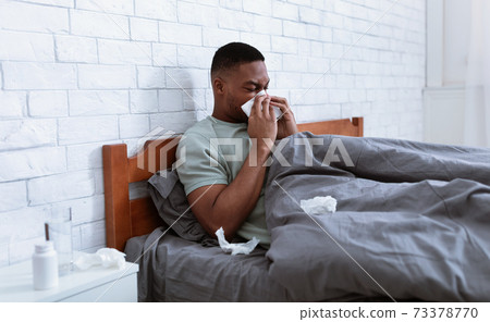 Sick Man Blowing Nose In Tissue Lying In Bed Indoor Sick Man Blowing Nose In Tissue Lying In Bed Indoor 73378770