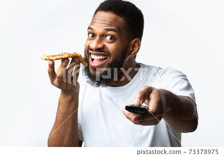 Black Man Eating Pizza And Watching TV Over White Background 73378975