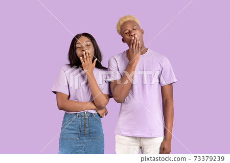 Tired black couple yawning with hands near mouths, feeling sleepy on lilac studio background Tired black couple yawning with hands near mouths, feeling sleepy on lilac studio background 73379239