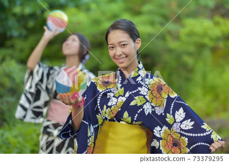 Two women in a yukata playing with a paper breeze Two women in a yukata playing with a paper breeze 73379295