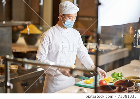 Concentrated man in chef uniform cutting peppers in kitchen Concentrated man in chef uniform cutting peppers in kitchen 73381333