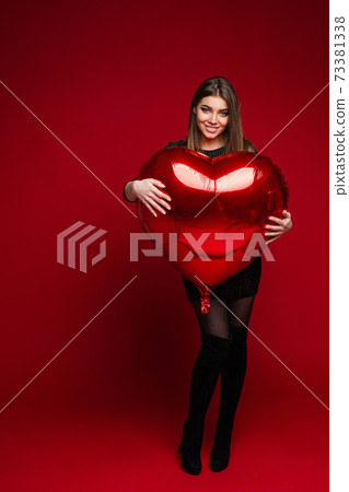 Happy attractive young woman posing against red Happy attractive young woman posing against red 73381338