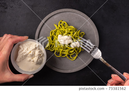 Female hands put straciatella on homemade pasta with pesto sauce 73381562