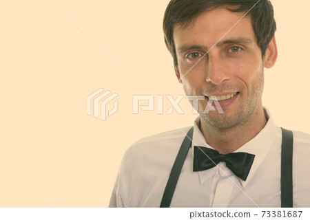 Close up of young happy man smiling while wearing suspenders and bow tie 73381687