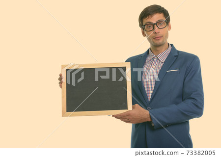 Studio shot of young handsome businessman wearing eyeglasses and holding blank blackboard 73382005