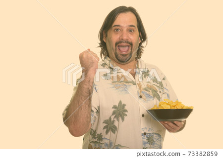 Happy fat Caucasian man smiling and looking motivated while holding bowl of chips 73382859