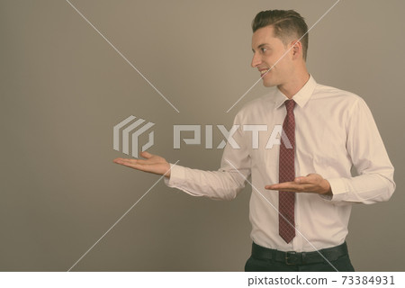 Young handsome businessman against gray background Young handsome businessman against gray background 73384931