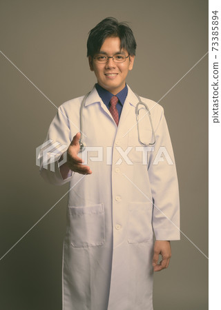Young handsome Asian man doctor wearing eyeglasses against gray background 73385894