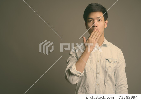 Young handsome Asian businessman wearing white shirt against gray background 73385994