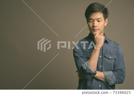 Young handsome Asian man wearing denim shirt against gray background 73386025