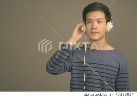 Young handsome Asian man listening to music against gray background 73386034
