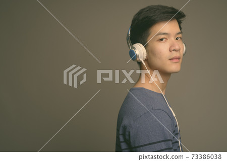 Young handsome Asian man listening to music against gray background 73386038