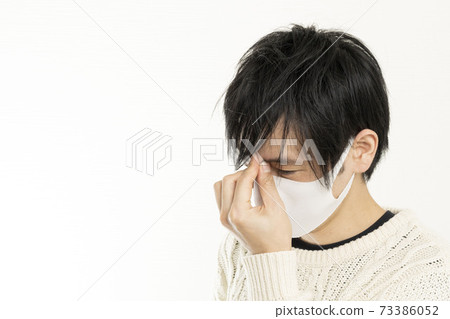 A man in a mask / holding his head with a headache / a single man who is sick / 73386052