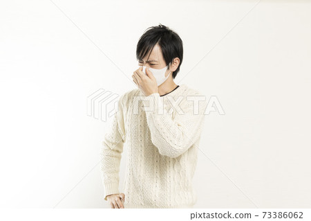 A man in a mask / holding his head with a headache / a single man who is sick / 73386062