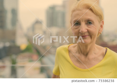 Beautiful senior woman with blond hair against view of the city 73386238