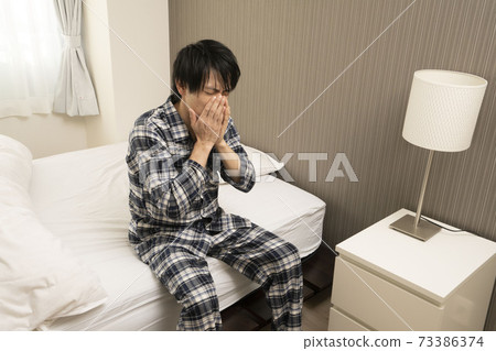 A man sneezing in his pajamas in the bedroom A man sneezing in his pajamas in the bedroom 73386374