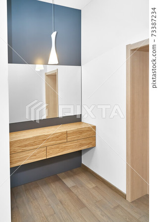 Floating cabinet of natural timber under large mirror in room Floating cabinet of natural timber under large mirror in room 73387234