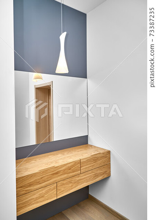 Floating cabinet of natural timber under large mirror in room 73387235