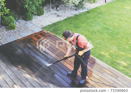 man cleaning terrace with a power washer - high water pressure cleaner on wooden terrace surface 73390663