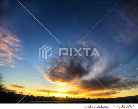 A landscape with gray clouds floating in the blue sky and a silhouette of the cityscape where you can see the sunset at sunset 73390764