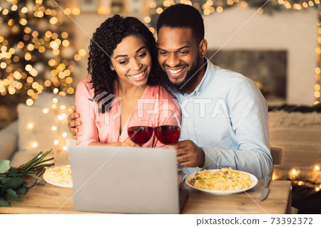 Black couple having videocall using laptop drinking wine Black couple having videocall using laptop drinking wine 73392372