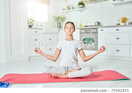 Positive vibes. Sporty relaxed latin teenage girl wearing sportswear practicing yoga, sitting in Lotus pose. Home interior background Positive vibes. Sporty relaxed latin teenage girl wearing sportswear practicing yoga, sitting in Lotus pose. Home interior background 73392855
