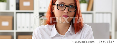Calm red woman working on notebook in office Calm red woman working on notebook in office 73394137