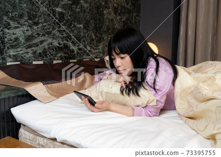 A woman watching a video on her smartphone in bed A woman watching a video on her smartphone in bed 73395755