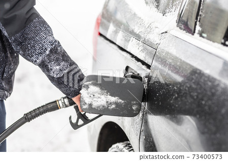 An open fuel tank with gas pistol in it held my a male in snowy winter 73400573