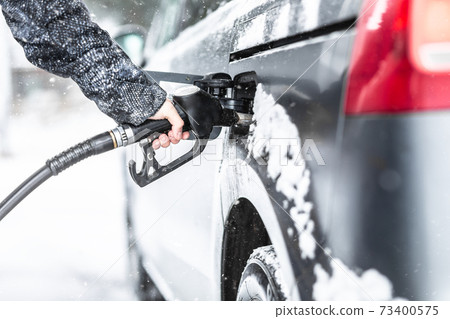 Male hand holding fuel pistol during gasoline refill in his minivan in cold winter Male hand holding fuel pistol during gasoline refill in his minivan in cold winter 73400575