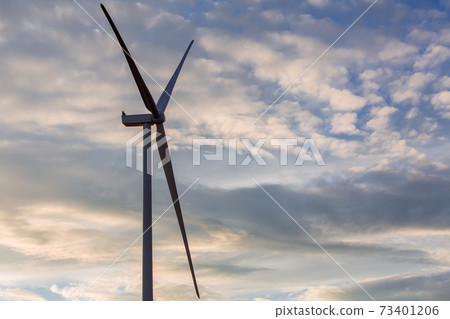 wind turbine offshore windmill of white color made of iron with blades side view against a blue sky with clouds on sunset, alternative electricity preserving nature. 73401206