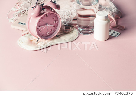 Alarm clock, eye mask, pills and glass of water on pink background. Insomnia or depression treatment for sleepless nights, copy space 73401379