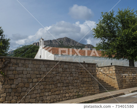View of old white red roof church Chiesa di Santa Maria over stone wall in small coastal village Santa Maria Navarrese, Sardinia, Italy, Summer sunny day. View of old white red roof church Chiesa di Santa Maria over stone wall in small coastal village Santa Maria Navarrese, Sardinia, Italy, Summer sunny day. 73401580