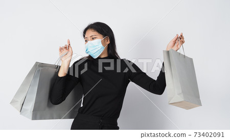 Covid 19 and shopping concept. Asian woman wearing face mask hold shopping bag. Girl and paper bag represent shopping during coronavirus crisis or covid19 outbreak. shopper and virus mask. white BG. Covid 19 and shopping concept. Asian woman wearing face mask hold shopping bag. Girl and paper bag represent shopping during coronavirus crisis or covid19 outbreak. shopper and virus mask. white BG. 73402091