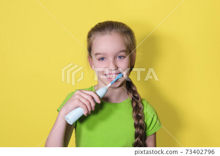 Teenager girl brushes her teeth on yellow background. Child girl in green t-shirt uses an electric toothbrush 73402796