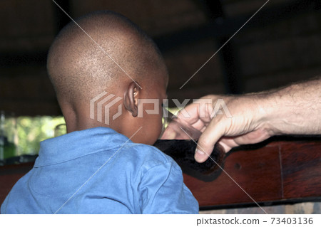 Black boy drinks a drink from a glass held by a white man's hand. 73403136