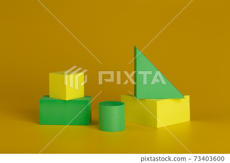 Duotone geometric still life with yellow and green figures against dark yellow background 73403600