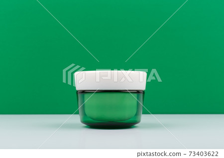 Green glass cream jar with white cap on white table against green background with space for text Green glass cream jar with white cap on white table against green background with space for text 73403622