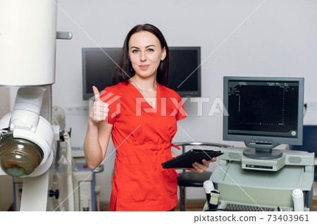 Close up of pretty Caucasian woman doctor standing in front of ultrasound and lithotripter machines and showing thumb up. Safety non-invasive stone treatment, extracorporeal shock wave lithotripsy Close up of pretty Caucasian woman doctor standing in front of ultrasound and lithotripter machines and showing thumb up. Safety non-invasive stone treatment, extracorporeal shock wave lithotripsy 73403961