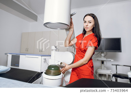 Portrait of young attractive woman doctor, looking at camera, standing near modern ultrasonic lithotriptor, while preparing for extracorporeal shock wave therapy in modern urology center Portrait of young attractive woman doctor, looking at camera, standing near modern ultrasonic lithotriptor, while preparing for extracorporeal shock wave therapy in modern urology center 73403964