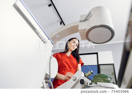 Bottom view of young attractive Caucasian female doctor in red uniform, working with modern lithotripter equipment for treatment of kidney stones. Non-invasive extracorporeal shock wave lithotripsy Bottom view of young attractive Caucasian female doctor in red uniform, working with modern lithotripter equipment for treatment of kidney stones. Non-invasive extracorporeal shock wave lithotripsy 73403966