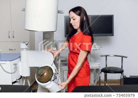 Portait of pretty confident focused Caucasian female doctor, wearing red medical uniform, working in modern clinic with ultrasonic lithotripter machine. Kidney stones treatment concept Portait of pretty confident focused Caucasian female doctor, wearing red medical uniform, working in modern clinic with ultrasonic lithotripter machine. Kidney stones treatment concept 73403979