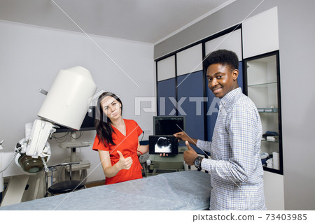 Happy doctor and patient in modern urology clinic. Young female doctor and her male african patient, holding tablet pc with ultrasound scan, smiling to camera and showing thumbs up Happy doctor and patient in modern urology clinic. Young female doctor and her male african patient, holding tablet pc with ultrasound scan, smiling to camera and showing thumbs up 73403985