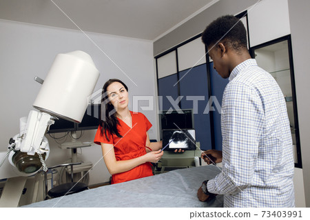 Young female caucasian doctor in modern clinic, holding tablet pc and showing to her male african patient ultrasound scan of kidneys and internal organs and explaining ways of treatment Young female caucasian doctor in modern clinic, holding tablet pc and showing to her male african patient ultrasound scan of kidneys and internal organs and explaining ways of treatment 73403991