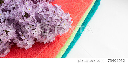 A stack of colorful bath towels with a sprig of lilac on a light background. Hygiene, fabric, spa and textile concept 73404932