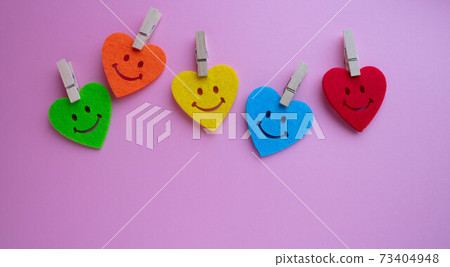 Bright hearts with smiles and small clothespins on a pink background. At the bottom is a place for your text 73404948