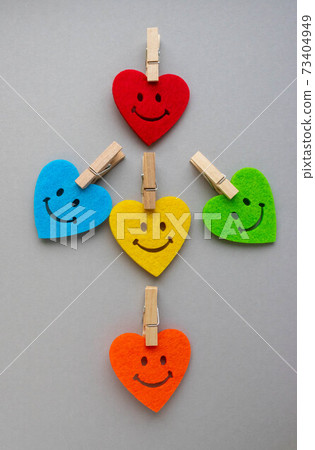 Vertical Valentine's day background with beautiful handmade toy hearts isolated on gray background.Bright hearts with smiles and small clothespins on a gray background 73404949