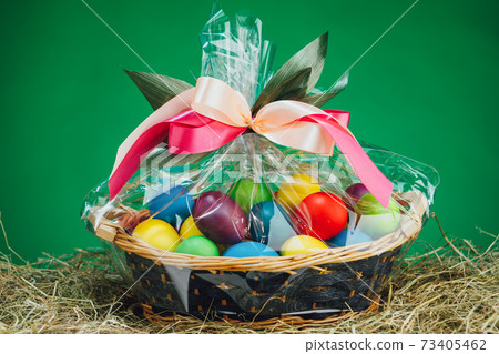 Easter gift basket with multicolor eggs, green background Easter gift basket with multicolor eggs, green background 73405462