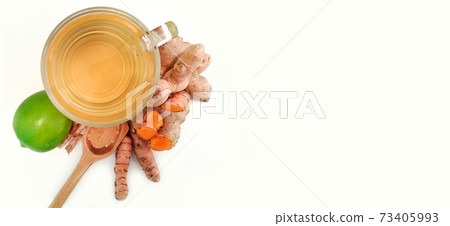 ginger and turmeric tea in glass cup next to lemon, cinnamon wooden spoon on white background with copy space ginger and turmeric tea in glass cup next to lemon, cinnamon wooden spoon on white background with copy space 73405993